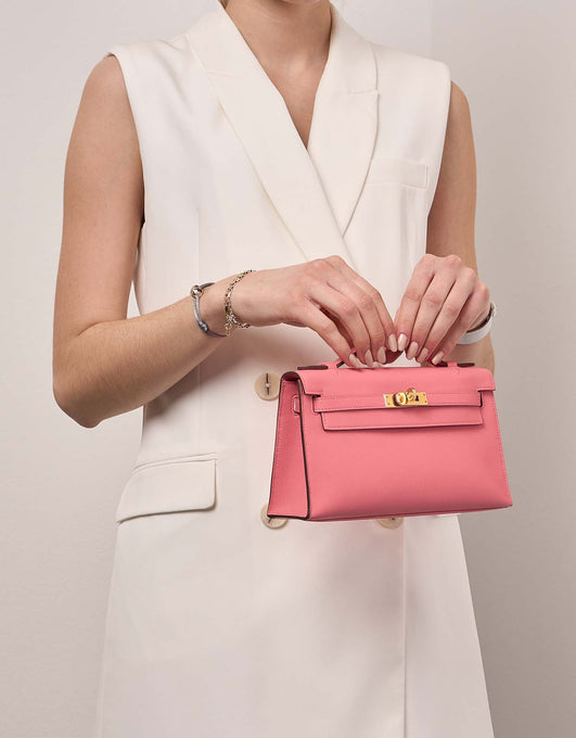 Woman holding Hermes Kelly Pochette Rose-Azalee handbag
