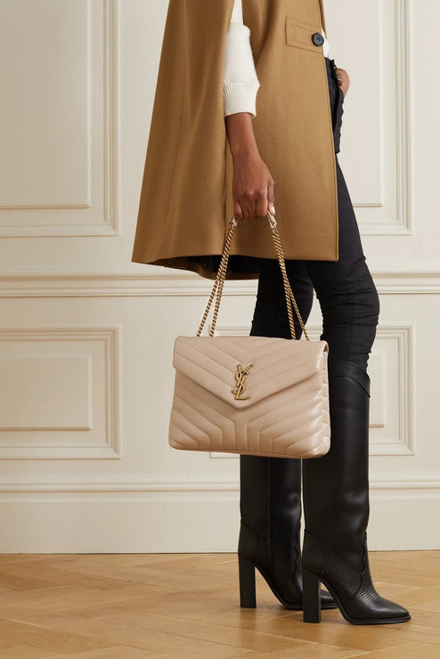 Woman holding a beige Saint Laurent Quilted handbag with gold chain strap in front of a neutral background