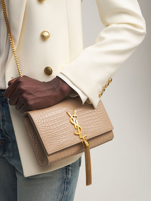 woman holding tan, crossbody Saint Laurent with gold chain strap and gold tassel